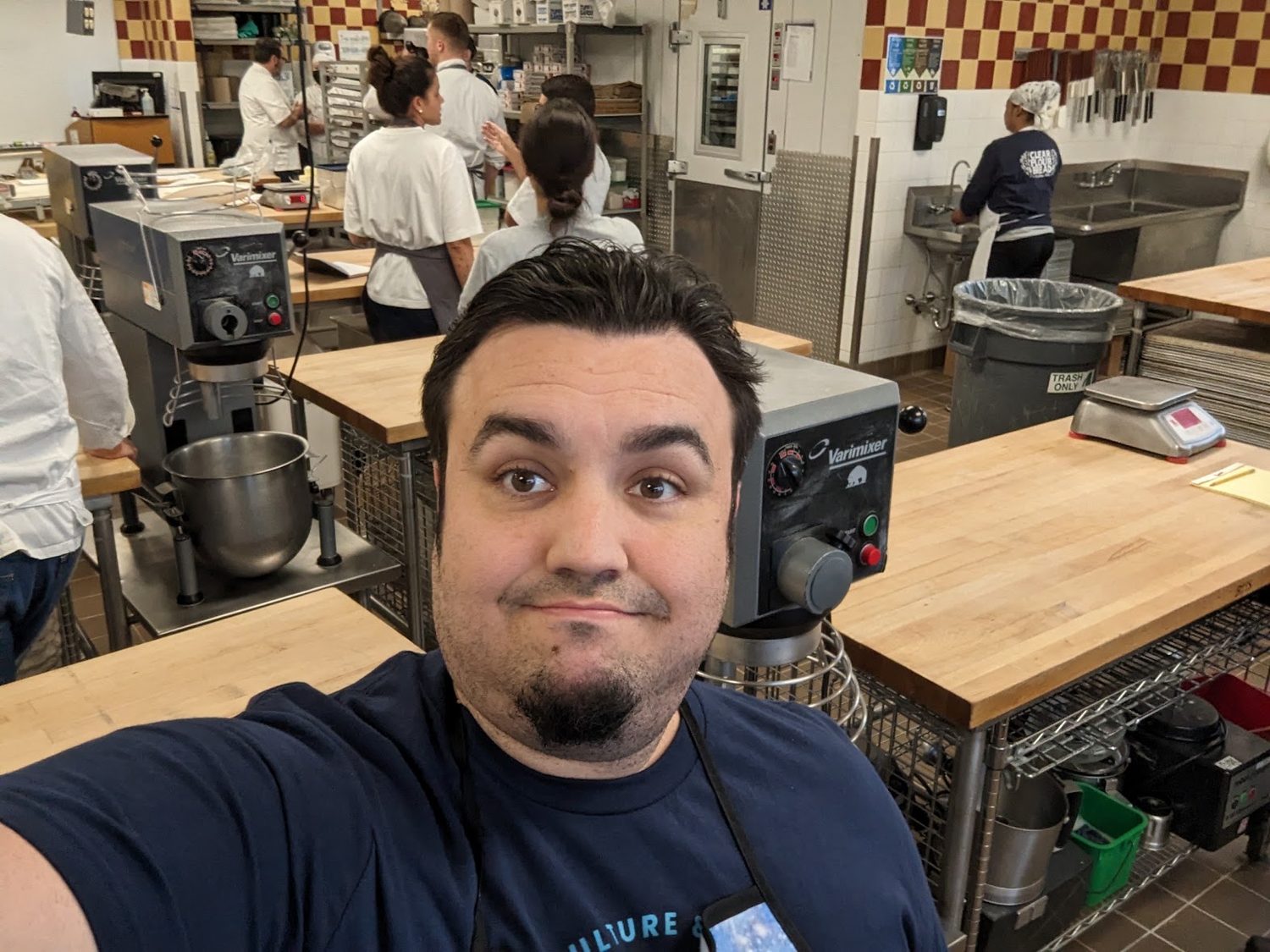 Allen in a busy teaching kitchen at Camp Bread, spiral mixers and bakers at work behind him