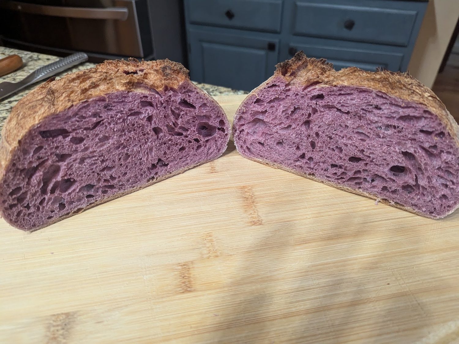 A sourdough loaf cut in half showing a deep purple crumb with an open irregular structure